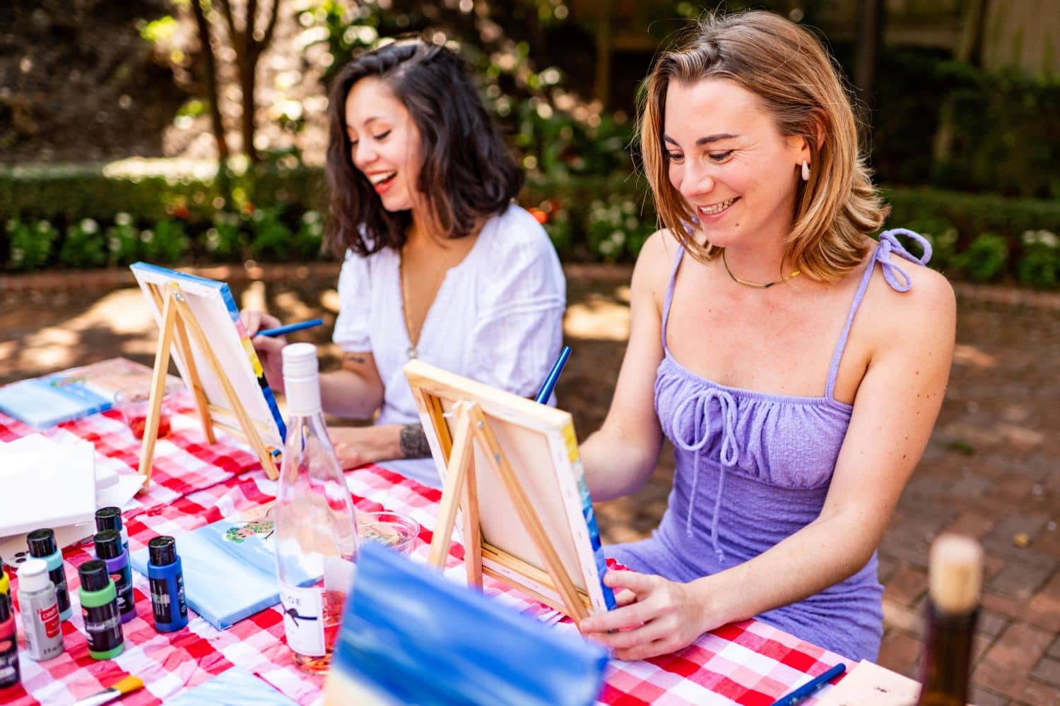 Two women painting outside and drinking wine.