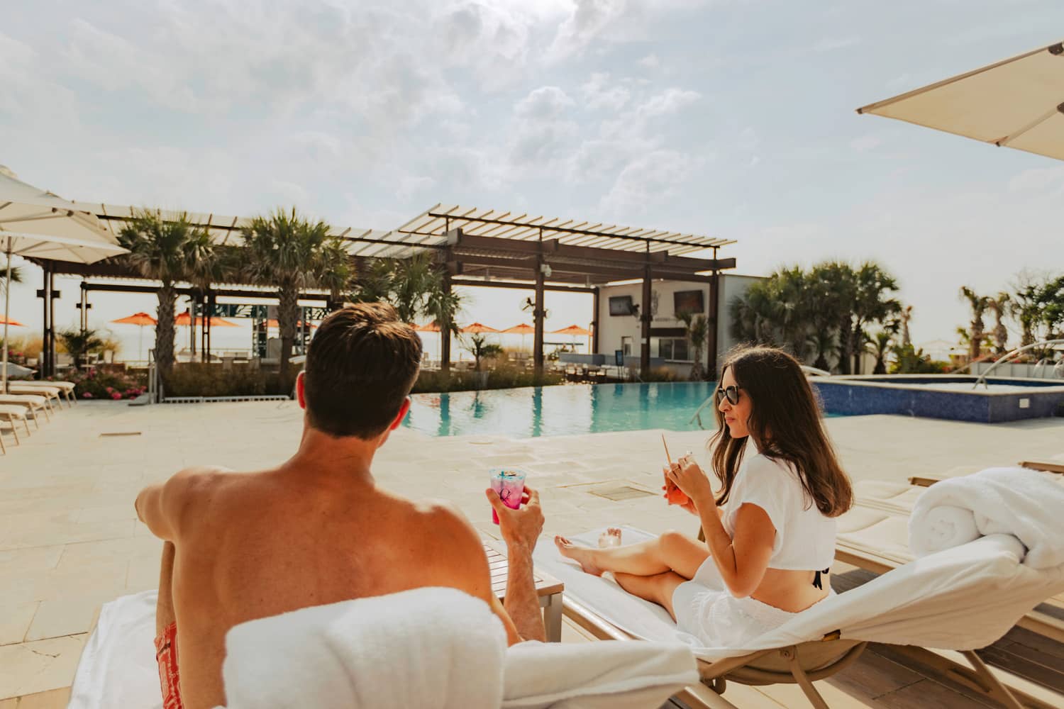 A couple sitting poolside with drinks in hand.