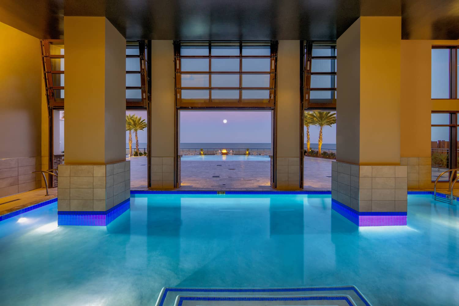 An indoor pool with a view of the beach and moon at night.
