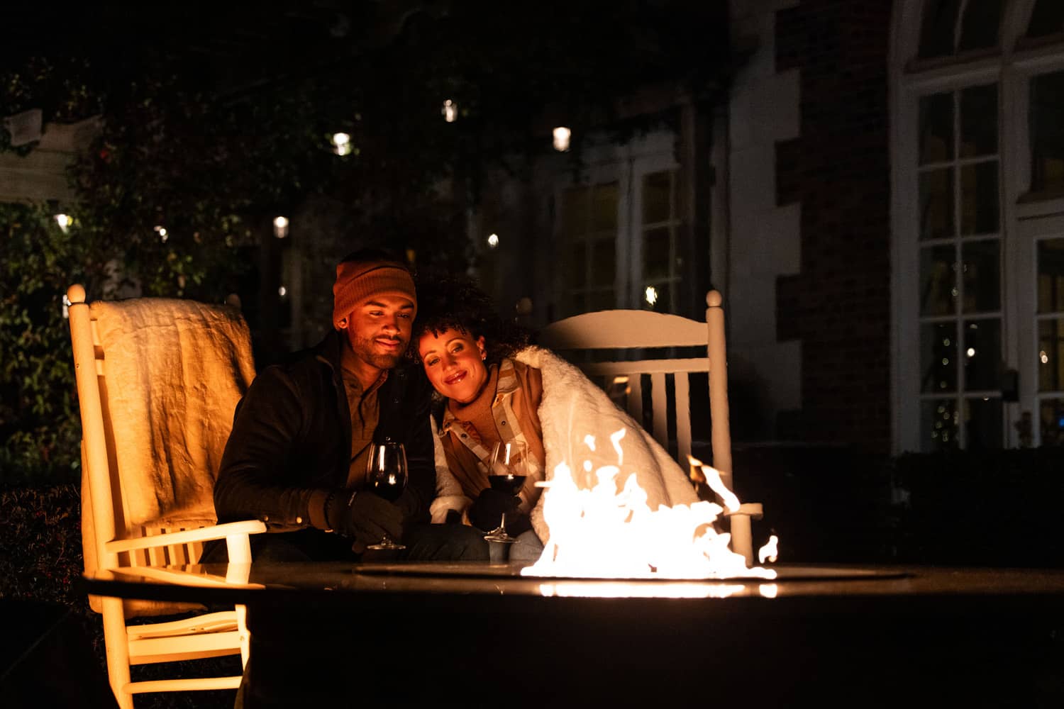 A couple sharing drinks next to a firepit at night