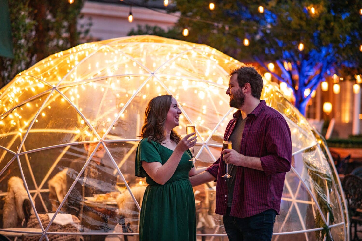 A couple embracing outside of a winter themed igloo while holding champagne