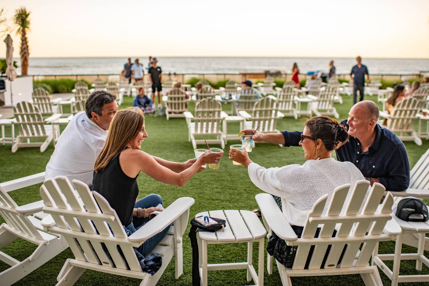 A group of people sharing drinks in chairs next to the ocean