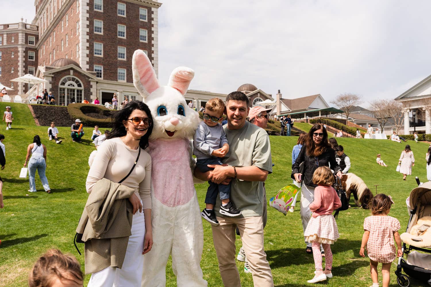 A family posing for a photo with the Easter Bunny on a green lawn