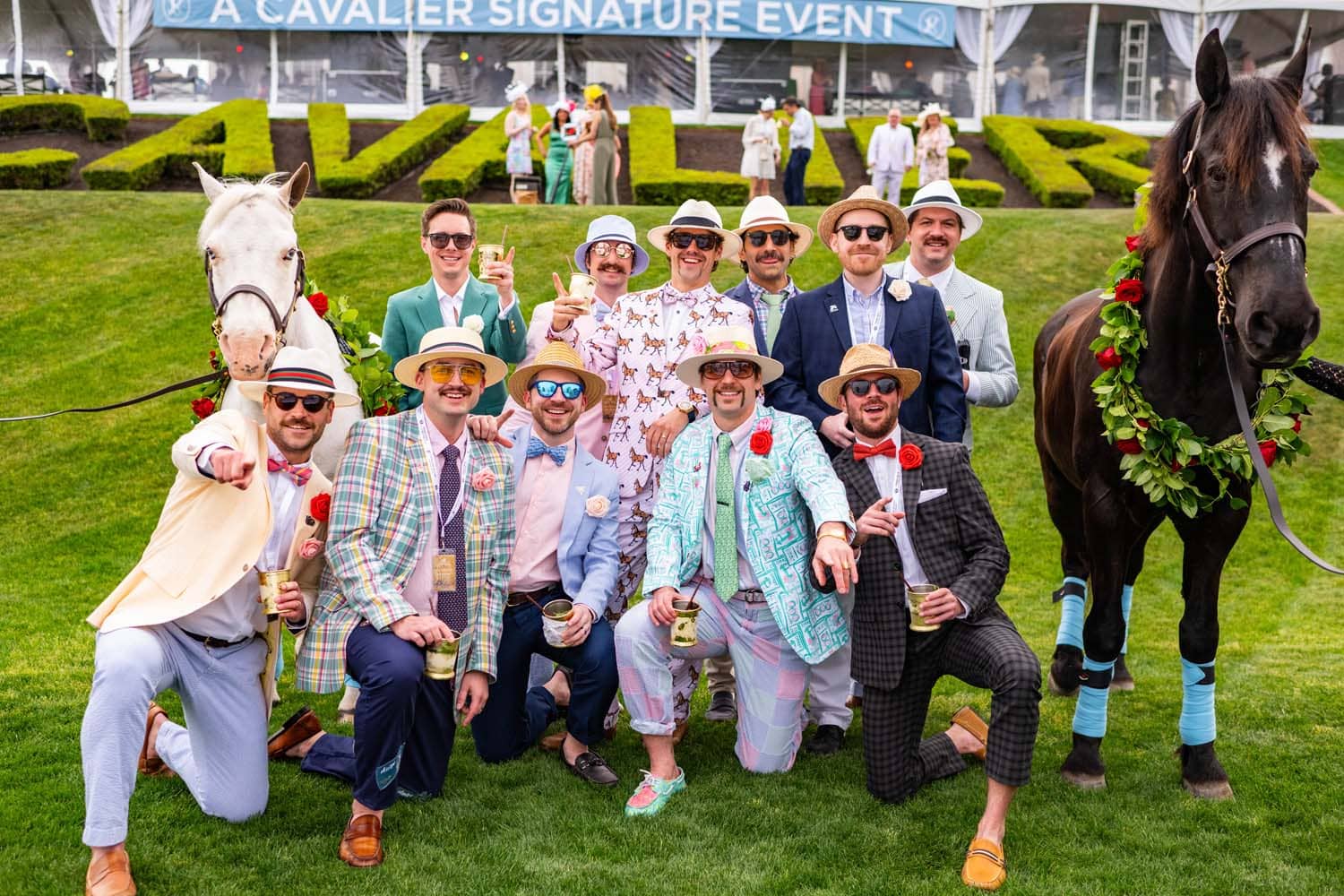 A group of well-dressed men posing for photos in front of a racing horse
