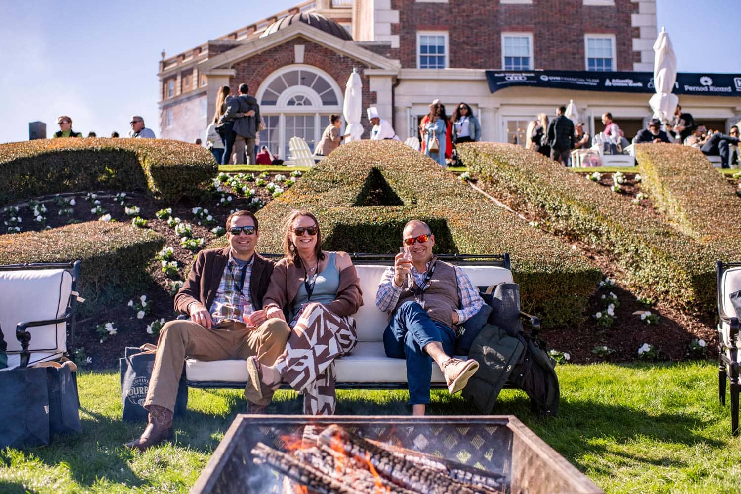 Three people sitting outside on a lawn next to a fire