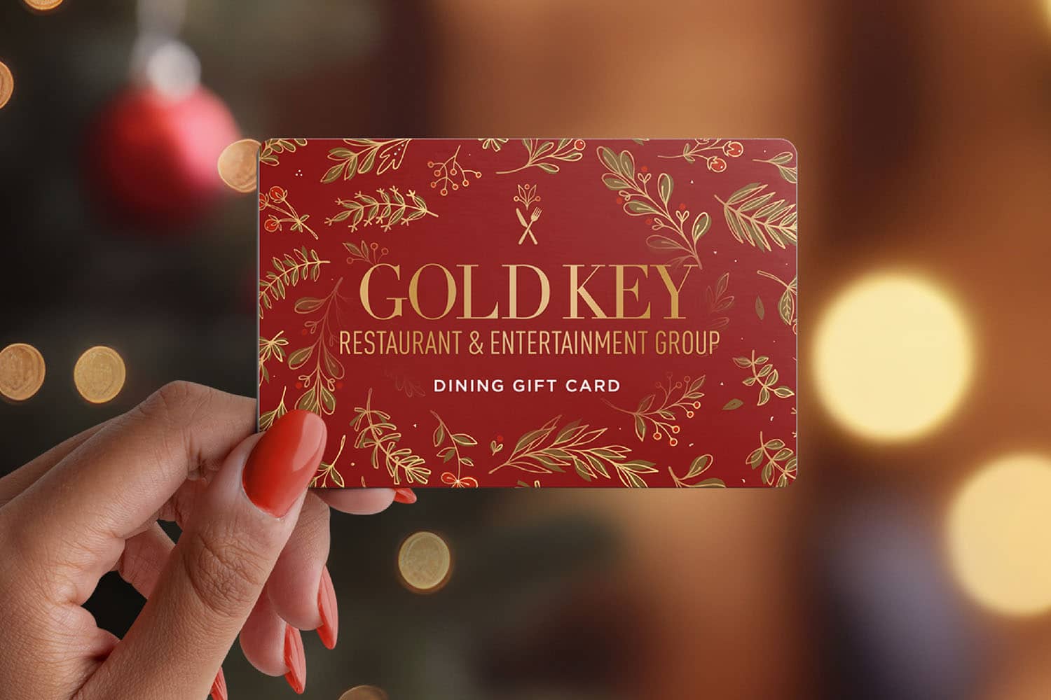 A holiday gift card held in a hand in front of holiday decorations.