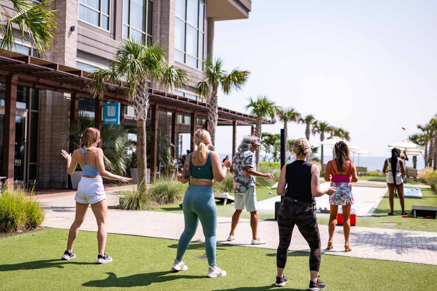 A group dancing outside on a lawn next to the beach