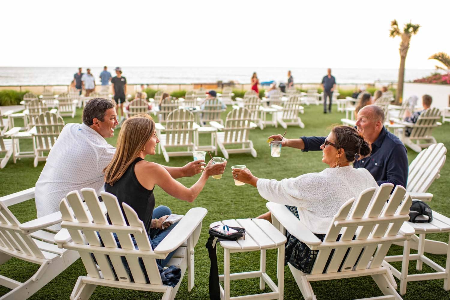A group of four people sitting in lawn chairs outside next to the beach at Tulu Seaside Bar & Grill