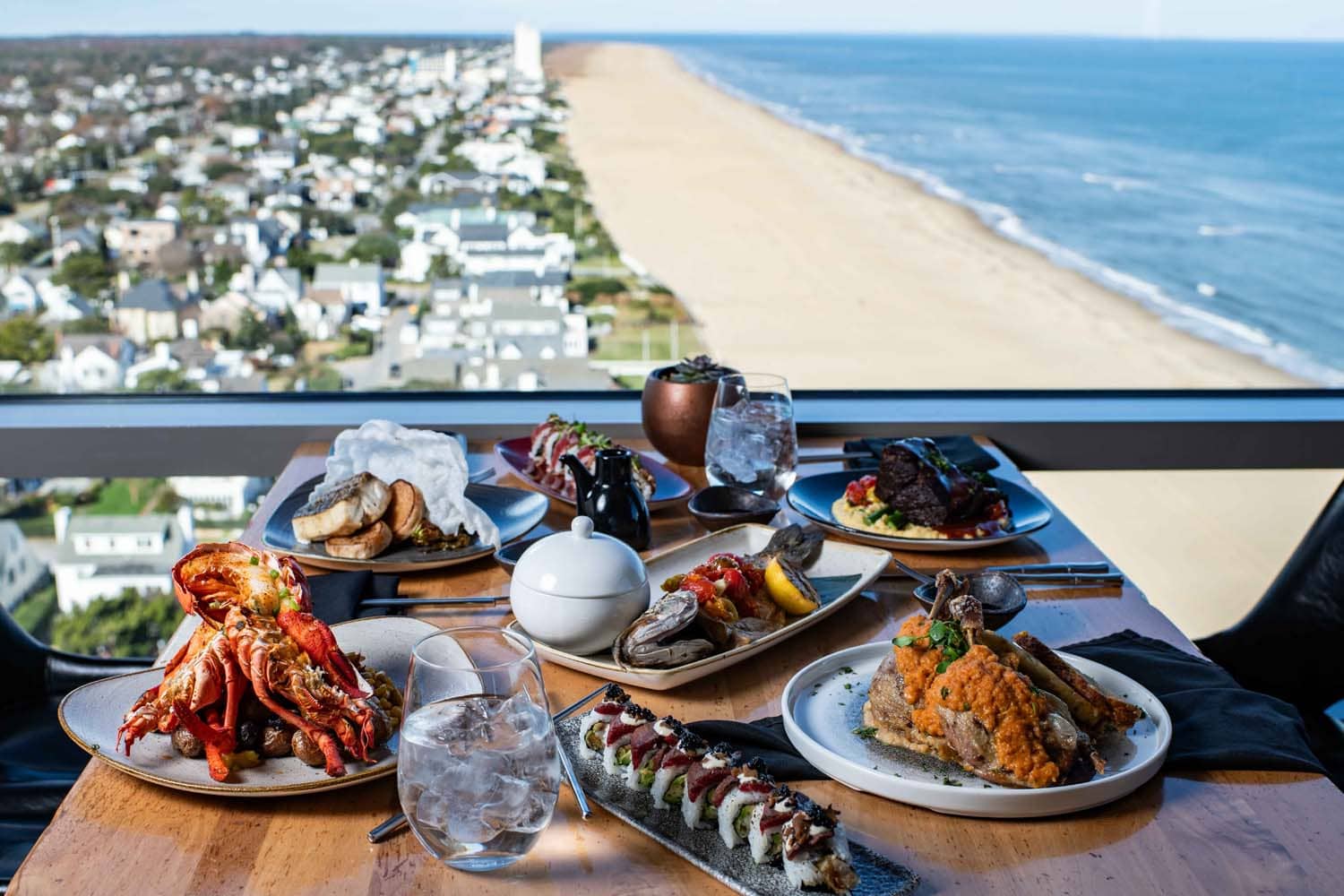 A variety of plated meals and drinks on a table at Orion's Roof restaurant with ocean views
