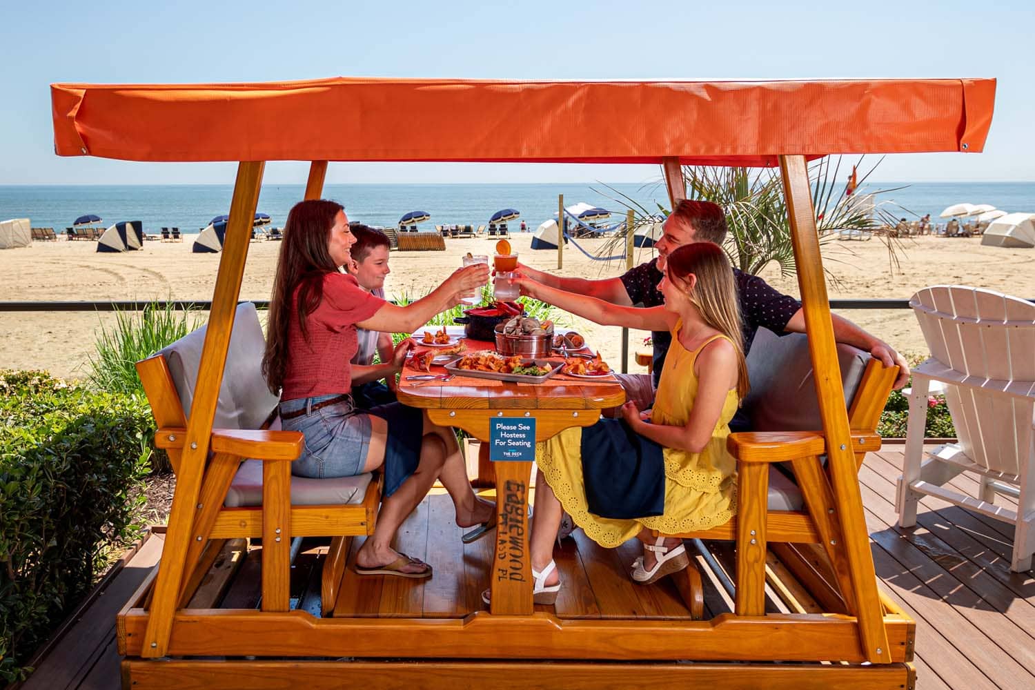 A family sharing a meal and toasting next to the beach at The Deck Seaside Bar & Grill