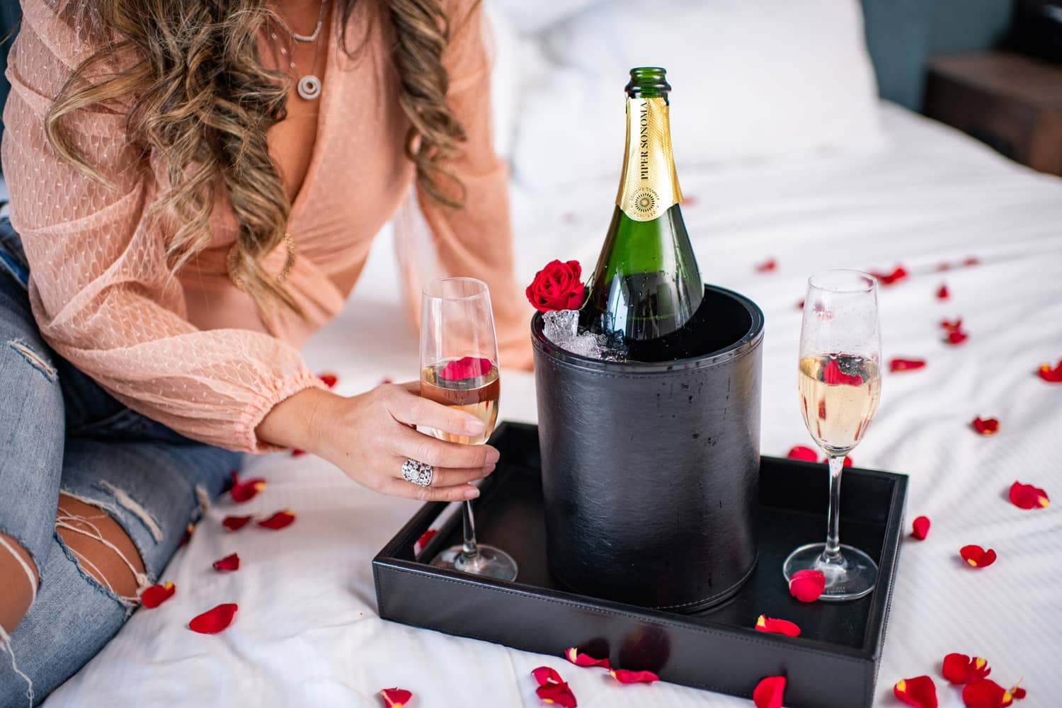 An in-room amenity offering of champagne and roses on a bed