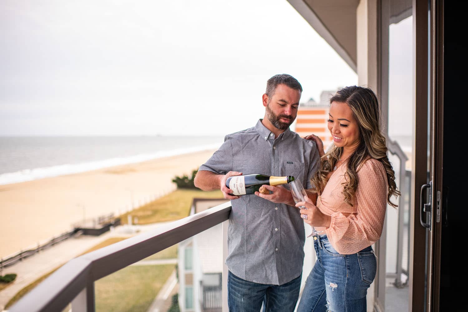 A couple drinking champagne on a hotel balcony overlooking the beach