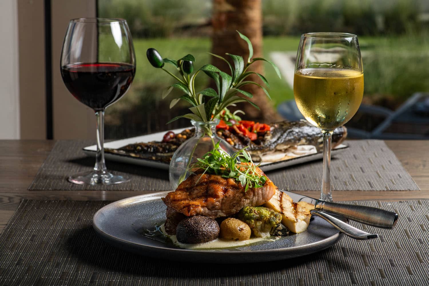 Grilled salmon entrée with vegetables, whole roasted fish, and glasses of red and white wine at Tulu Seaside Bar & Grill